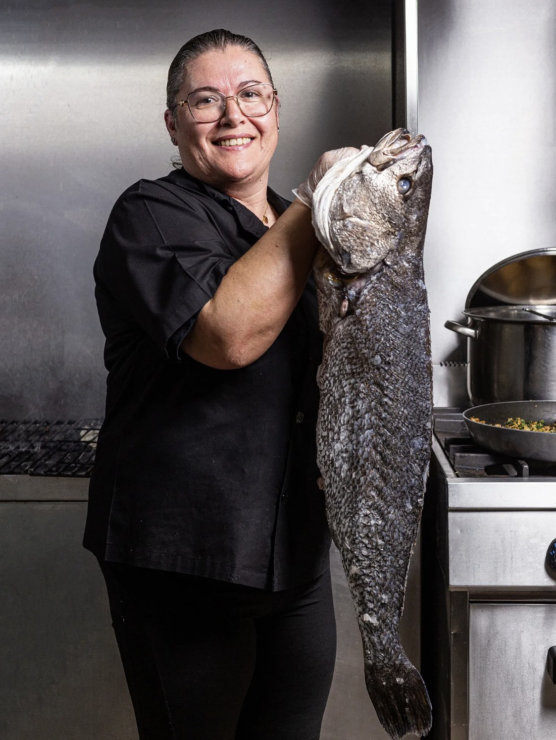 Cozinheira do S. Pedro na cozinha, a segurar uma corvina fresca acabada de chegar do mar.